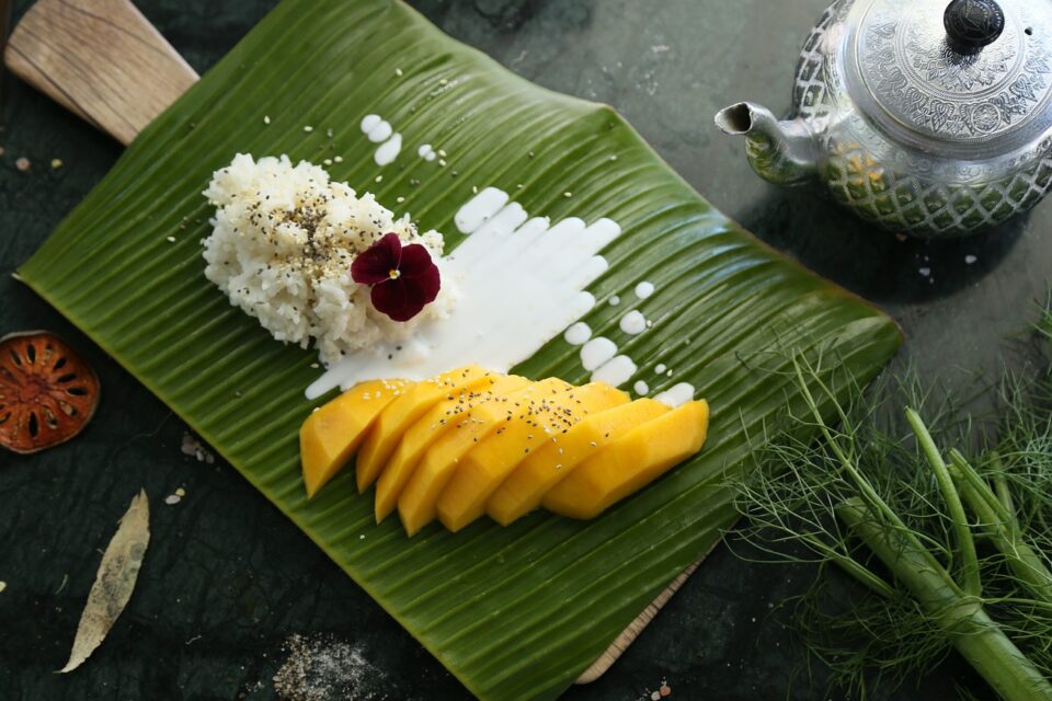 Mango sticky rice servito su foglia di banana, un dolce tradizionale veg-friendly tipico della cucina tailandese a Bangkok.