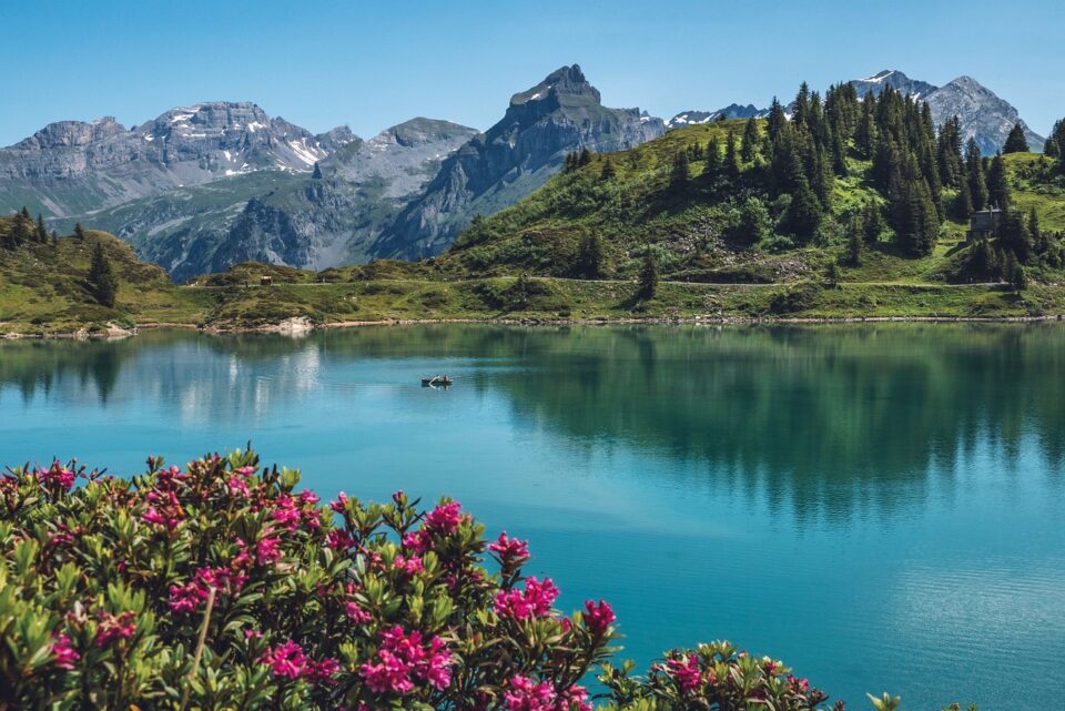 Nella primavera in Svizzera e Calabria, la natura regala scenari mozzafiato: un lago alpino svizzero riflette il cielo limpido tra cime ancora innevate.